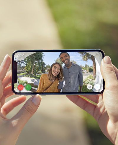 A phone in horizontal orientation held by two hands, with screen showing a live view in which there is a male and female with smile on their faces